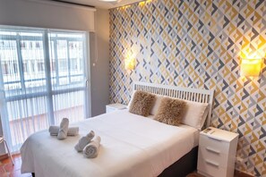A hotel room with a large bed, two bedside tables, a window with blinds, and a patterned wall. - ¡A pie de playa! Apartamento Cap Negret (Altea)