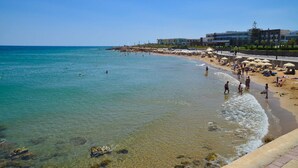 A beach with clear waters, people swimming, and beach umbrellas.
