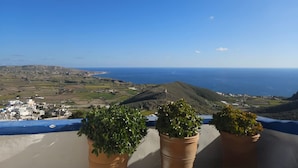 Un balcon orné de pots en terre cuite, donnant sur un paysage côtier avec des bâtiments et la mer.