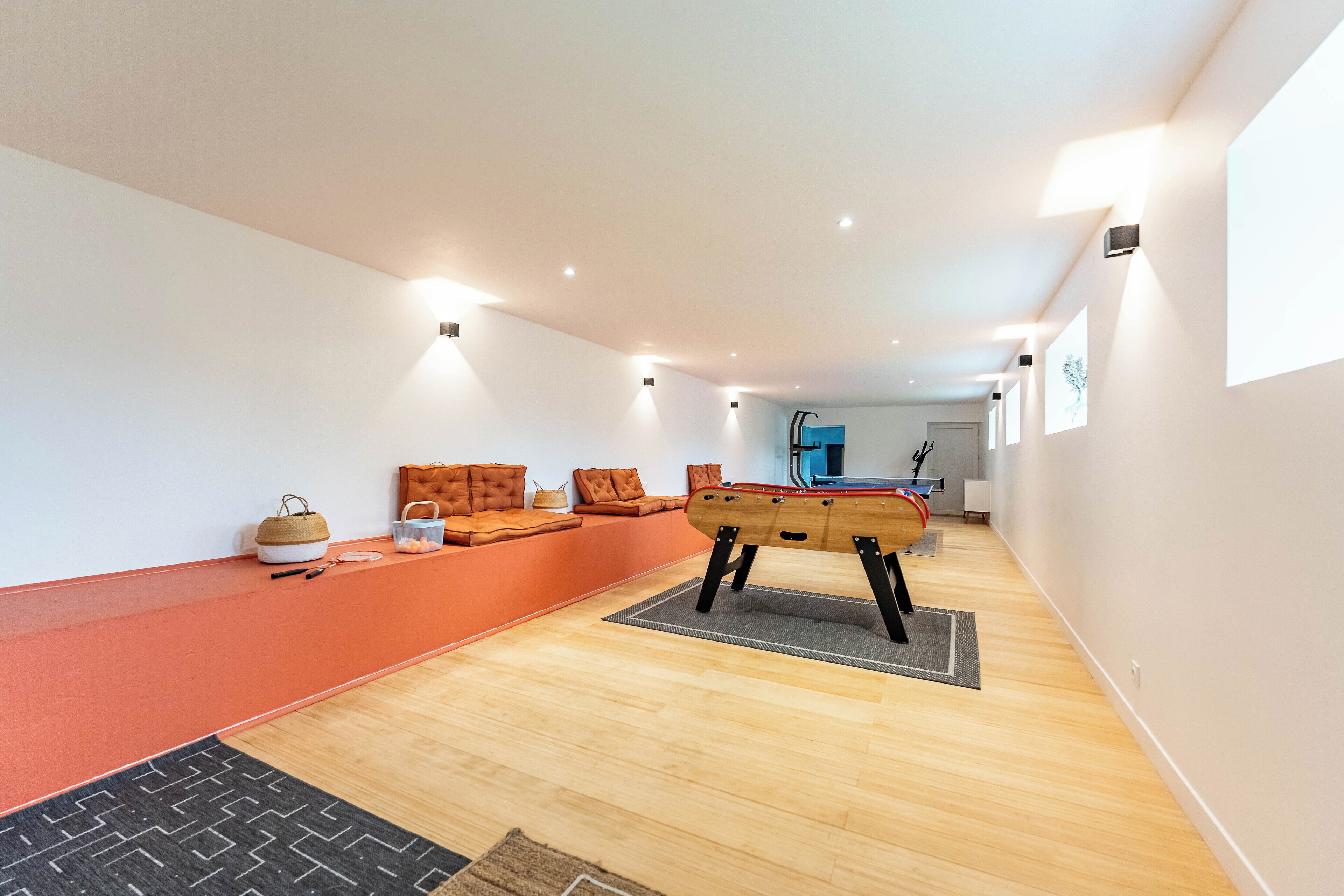 A modern living room with a wooden floor, orange seating area, and a pool table.