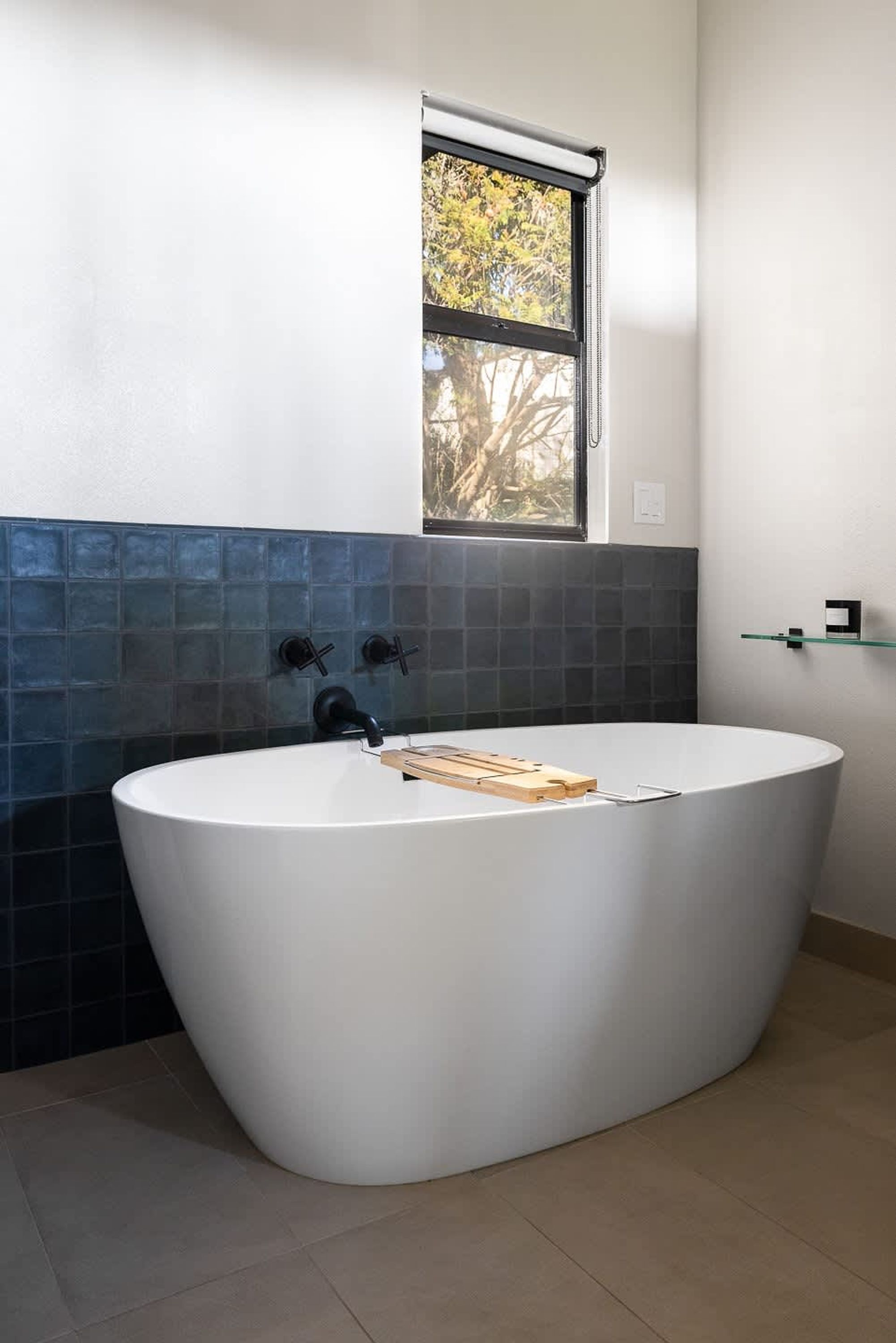 A modern bathroom with a freestanding bathtub, a window above the sink, and a tiled backsplash.