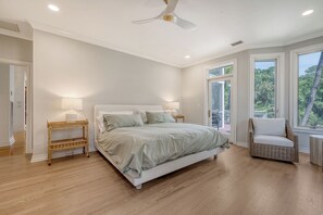 Une chambre dotée d’un grand lit, de deux tables de chevet, d’un ventilateur de plafond et d’une fenêtre donnant sur un paysage verdoyant.