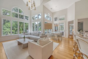 Een ruime woonkamer met een grote bank, salontafel en een eethoek met rieten stoelen.