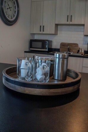 A kitchen counter with a tray holding glass mugs, a stainless steel mug, and a glass container. - L'Oasis de Nancy Summ (Rouyn-Noranda)
