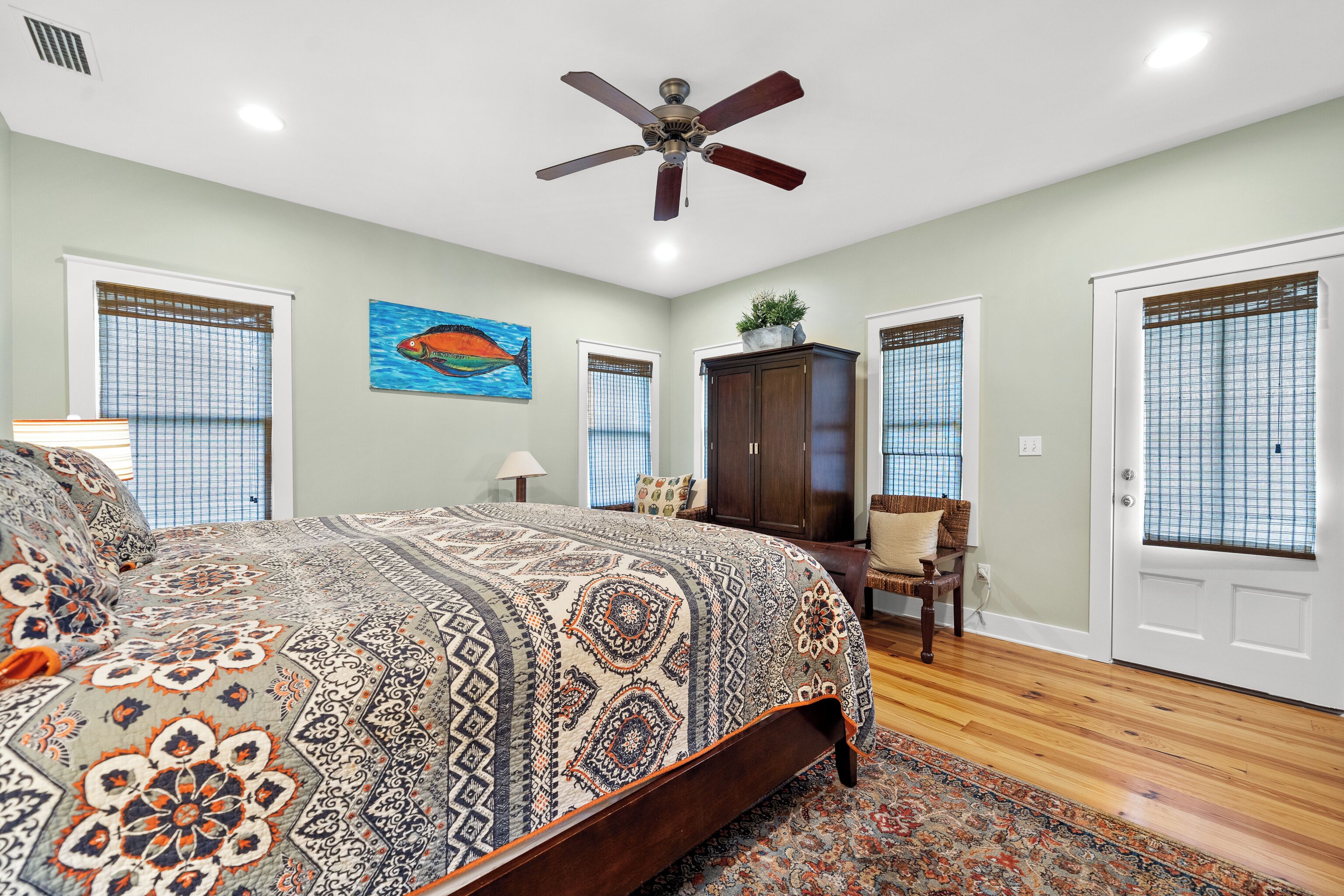 A bedroom with a large bed, a ceiling fan, and a fish painting on the wall.