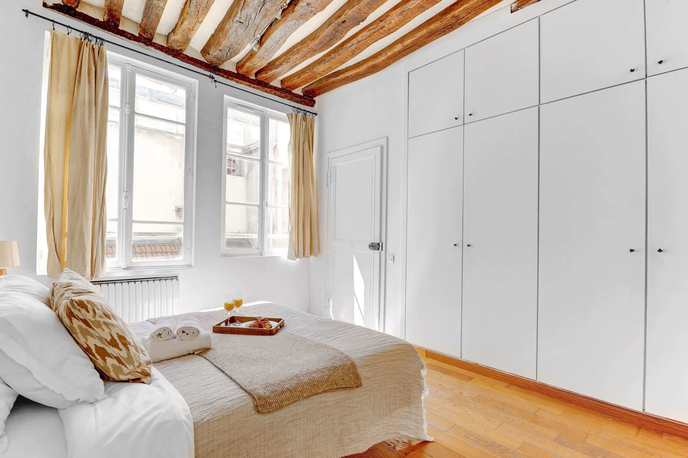 Ein Schlafzimmer mit Bett, Fenster mit Vorhängen, Kleiderschrank und Heizkörper.