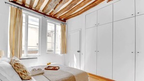 A bedroom with a bed, a window with curtains, a wardrobe, and a radiator. - Charming 1BR Near Notre-Dame & Latin Quarter (Paris)