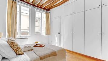 Ein Schlafzimmer mit Bett, Fenster mit Vorhängen, Kleiderschrank und Heizkörper.