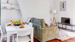A modern living room with a white table set for breakfast, a grey sofa, and a TV stand. - Charming 1BR Near Notre-Dame & Latin Quarter (Paris)