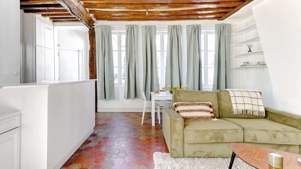 A cozy living room with a green sofa, wooden ceiling beams, a white rug, and a dining area with a table and chairs. - Charming 1BR Near Notre-Dame & Latin Quarter (Paris)