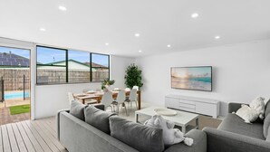 A modern living room with a pool view, a dining area, and a TV on the wall.