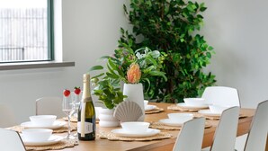A dining table set with white dishes, a bottle of wine, and a potted plant.