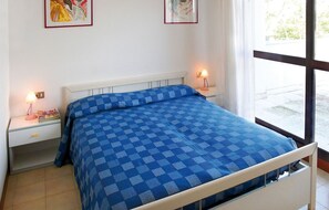 A bedroom with a checkered blue bedspread, white headboard, bedside tables with lamps, and framed artwork on the wall.