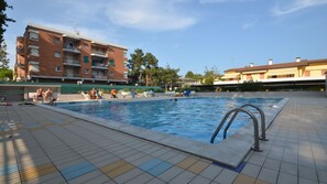 A swimming pool with tiled flooring and a metal ladder, surrounded by buildings and trees.