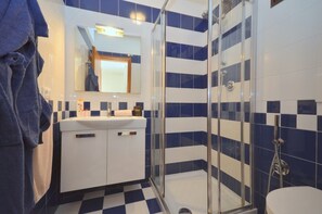 Une salle de bain avec un carrelage à motifs géométriques, une douche en verre et un lavabo blanc avec un miroir au-dessus.
