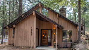 A wooden cabin with a front door, a chimney, and a large window. - RR015 | Lovely Ranch cabin nestled in the woodsy Central Oregon landscape. (Black Butte Ranch)