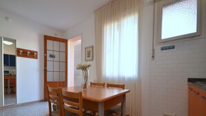Ein Essbereich mit einem Holztisch und Stühlen, einer Blumenvase und einem fenster mit Vorhängen.