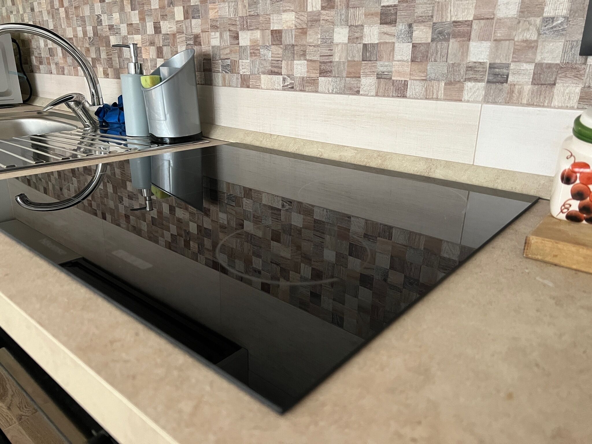 A kitchen with a black induction cooktop, a stainless steel sink, and a tiled backsplash.