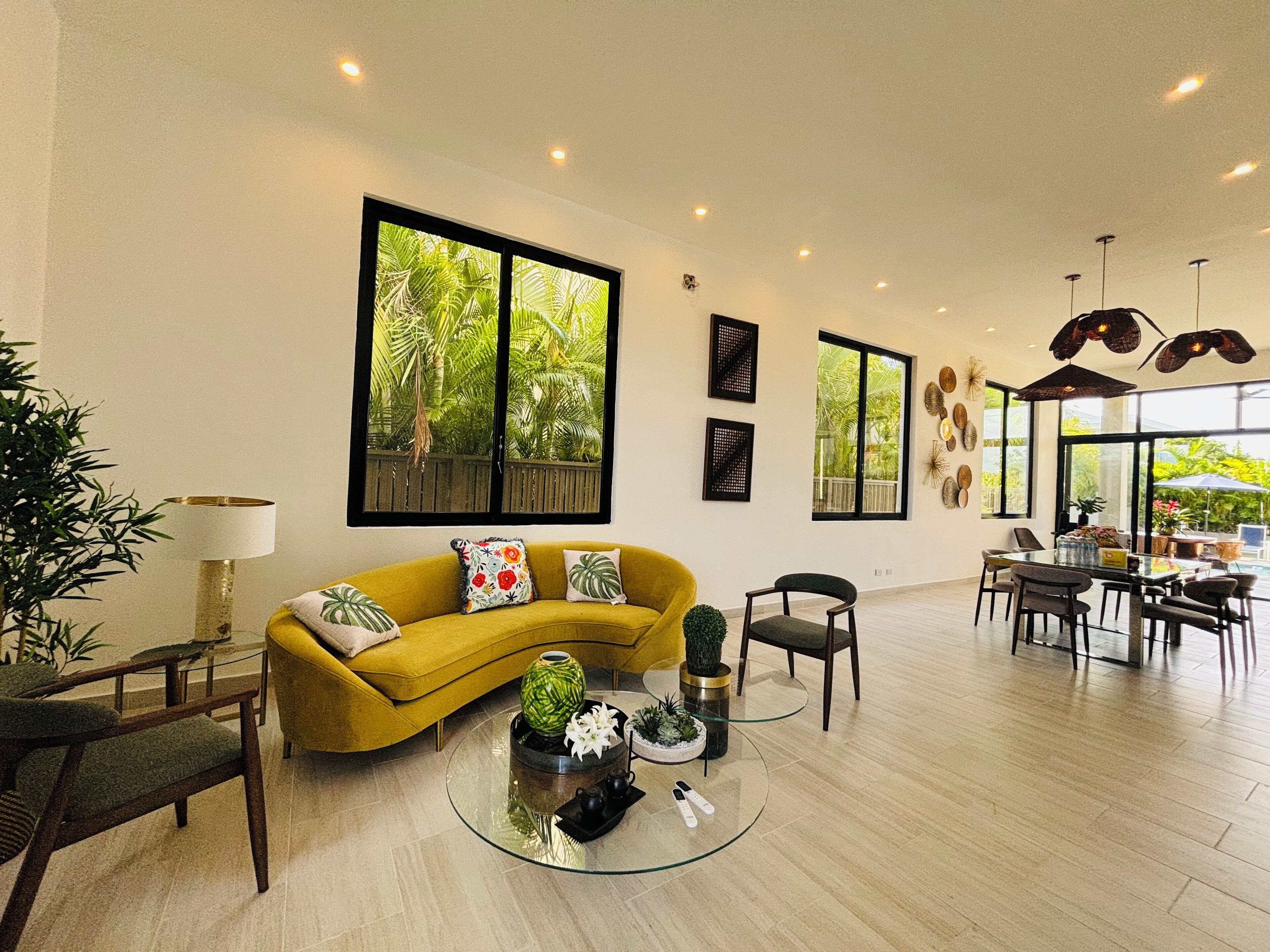 A modern living room with a yellow sofa, a glass coffee table, and a dining area with a table and chairs.