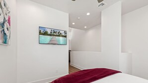Une chambre d’hôtel moderne avec un grand lit, un plaid rouge, un téléviseur à écran plat fixé au mur et un plancher en bois.