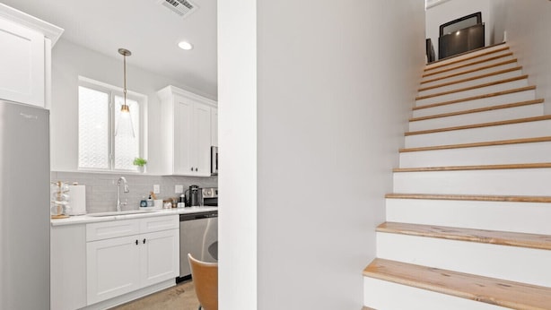 Une cuisine moderne avec des meubles blancs, un réfrigérateur en acier inoxydable et un escalier en bois.