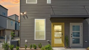 Un immeuble résidentiel de deux étages, doté d’un design moderne, avec une porte d’entrée munie d’un panneau de verre, un petit jardin devant, et un ciel dégagé en arrière-plan.