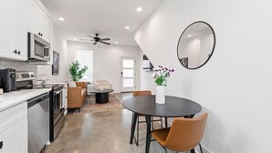 Une cuisine moderne avec des armoires blanches, un four à micro-ondes et une cuisinière. On y trouve un coin repas avec une table ronde et des chaises, ainsi qu'un ventilateur de plafond.
