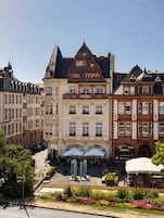Un hotel de estilo arquitectónico europeo clásico, con una entrada destacada que incluye un balcón y un cartel que dice 'HOTEL PORTA NIGRA VICTUS'.