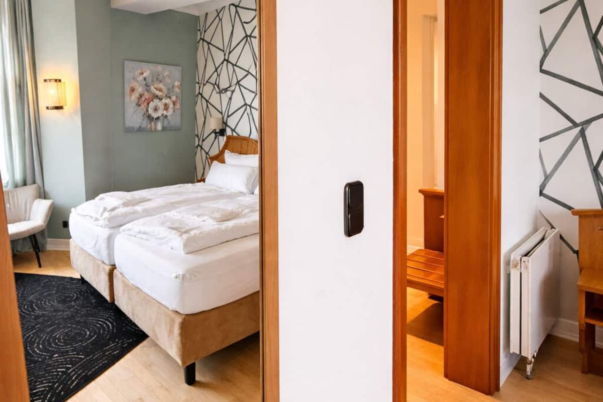 A modern hotel room with a large mirror, a bed, a desk, and a radiator.
