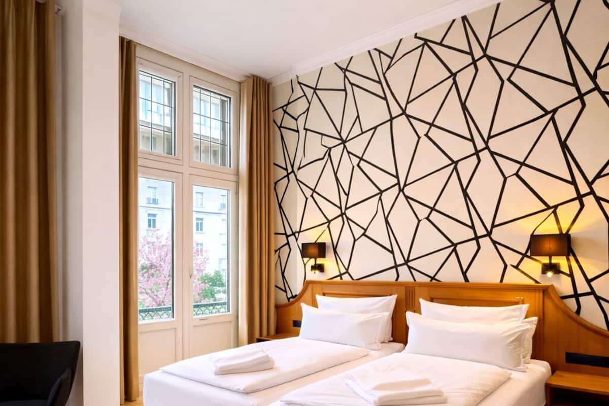 A hotel room with a double bed, a chair, a desk, and a geometric wall design.