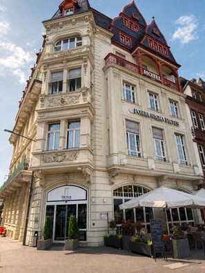 A historic building with ornate architecture, a prominent entrance, and a sign for 'Portia Nigravictus Hotel.' - Porta Nigra Victus (Trier)