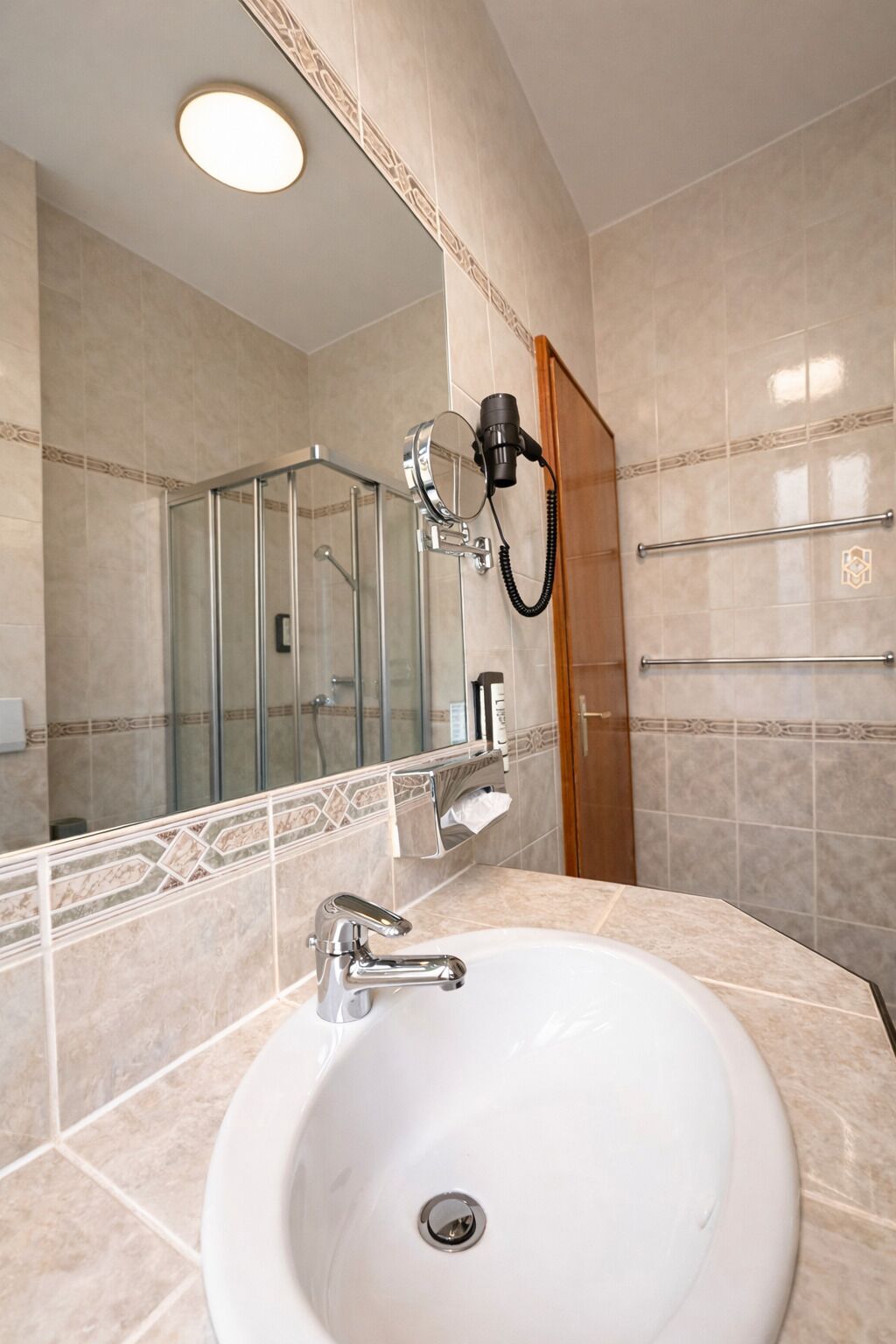 A bathroom with a white sink, a handheld mirror, a hairdryer, and a glass shower enclosure.