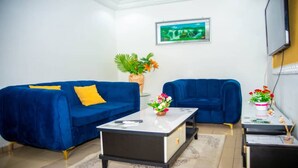 Un salon avec deux canapés bleus, une table basse, un téléviseur fixé au mur et une plante en pot.