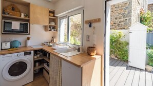 A compact kitchen with a washing machine, microwave, and wooden cabinets. - Nice duplex in Saint-Quay, a short walk to the bea (Saint-Quay-Portrieux)