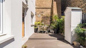 A narrow wooden deck with a table and chairs, surrounded by potted plants and a stone wall. - Nice duplex in Saint-Quay, a short walk to the bea (Saint-Quay-Portrieux)
