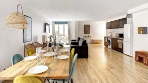 A modern kitchen with white appliances, a dining area with a wooden table and colorful chairs, and a living area with a sofa and a coffee table. - Spacious 4BDR in Buttes Chaumont pour 12 pers (Paris)