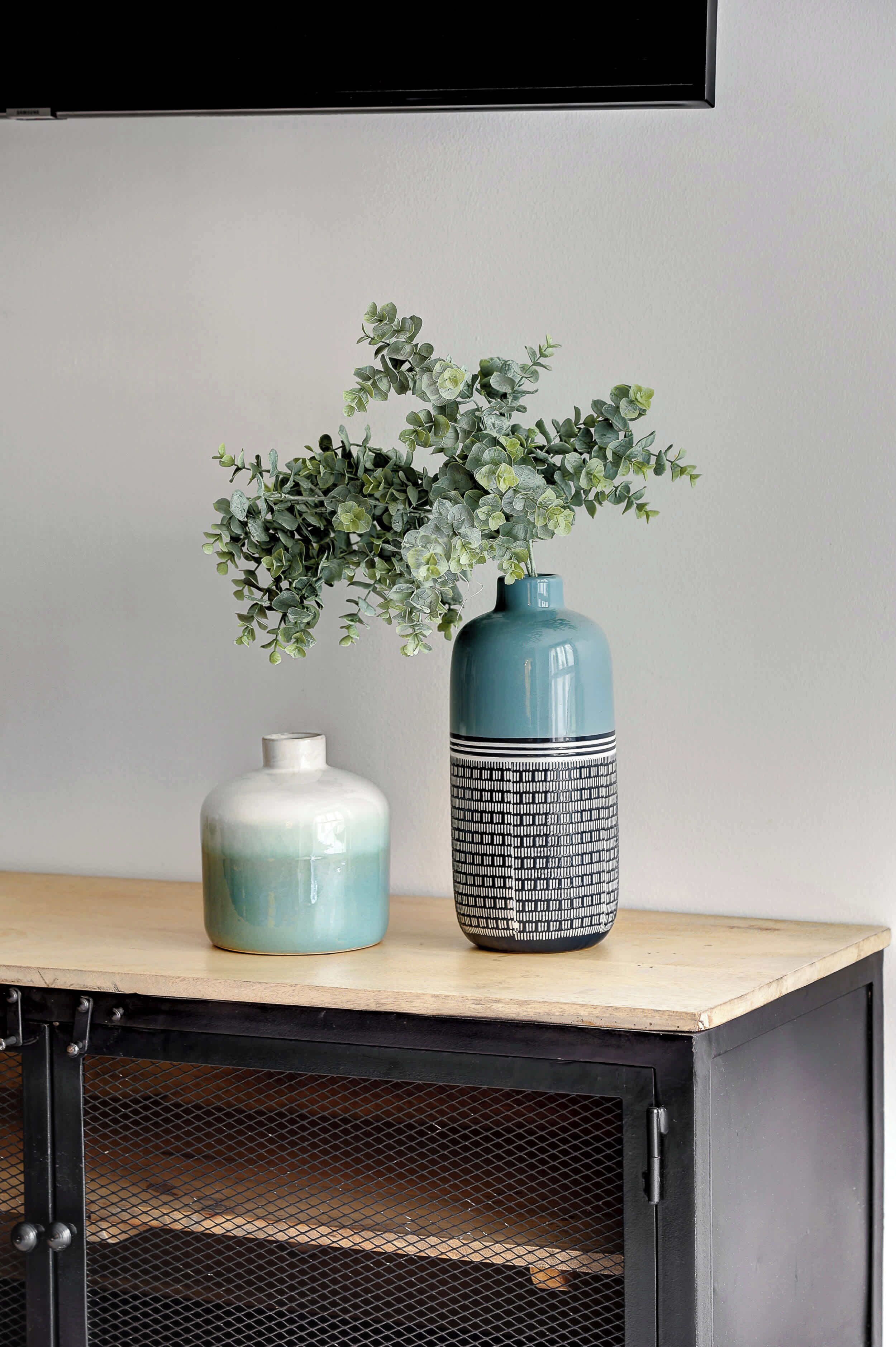 Twee vazen met planten op een houten tafel, tegen een muur.