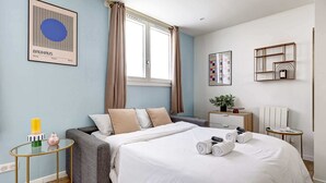 Ein modernes Hotelzimmer mit einem Bett, einem kleinen runden Tisch, einer Kommode und einem Spiegel an der Wand.