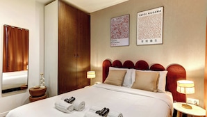 Ein Hotelzimmer mit einem großen Bett, zwei an der Wand befestigten Kunstwerken, einem Holzschrank und einem Nachttisch mit Lampe.