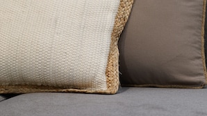 Ein graues Sofa mit zwei Kissen, eines weiß und eines braun, mit gewebtem Rand.