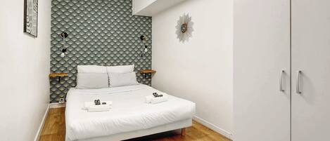 A neatly arranged bedroom with a bed, bedside tables, a wardrobe, and a patterned wall.