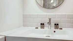 Un baño con un lavabo blanco, dos productos Kiehl's y un espejo redondo en la pared.