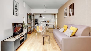 Una sala de estar moderna con un sofá, un televisor, un comedor y una cocina al fondo.