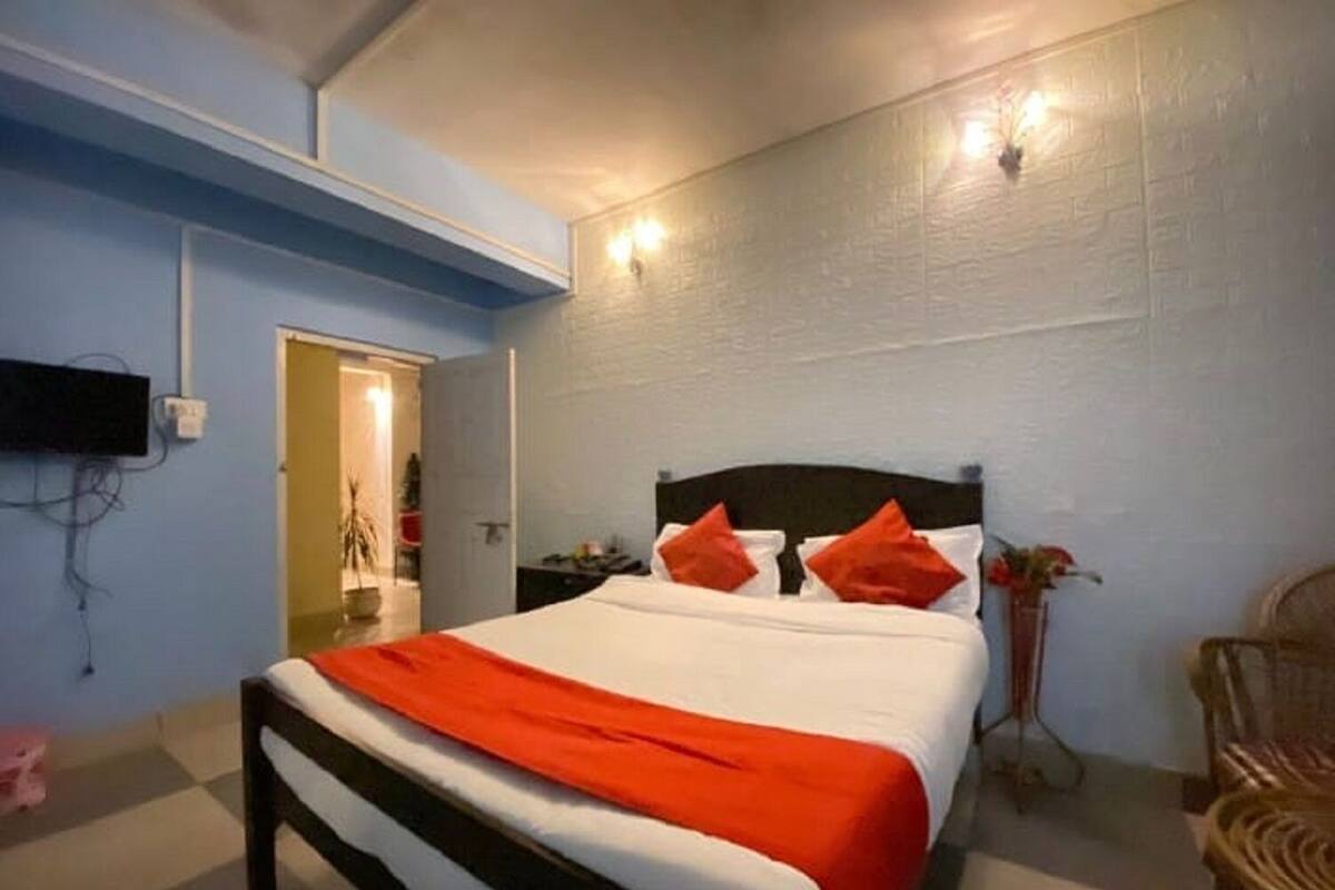 A bedroom with a bed, a nightstand, a chair, and a wall-mounted TV.
