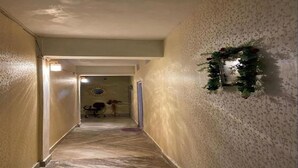 En smal hall med ett mattbeklätt golv, en dörr längst in och en väggmonterad spegel dekorerad med en blomsterkrans.