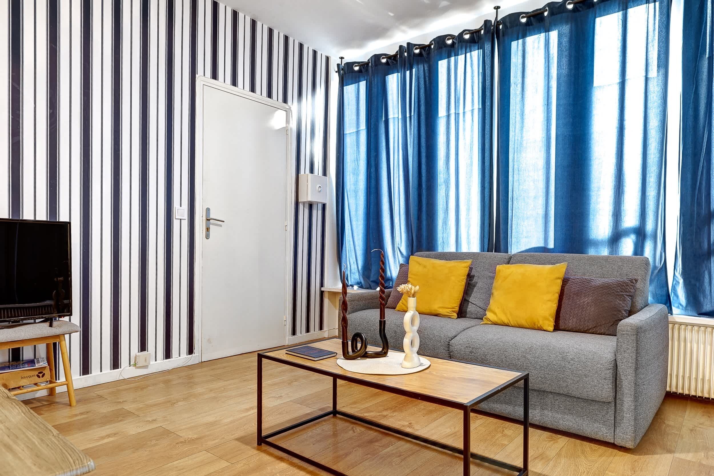 A modern living room with a grey sofa, wooden coffee table, and a striped wall.