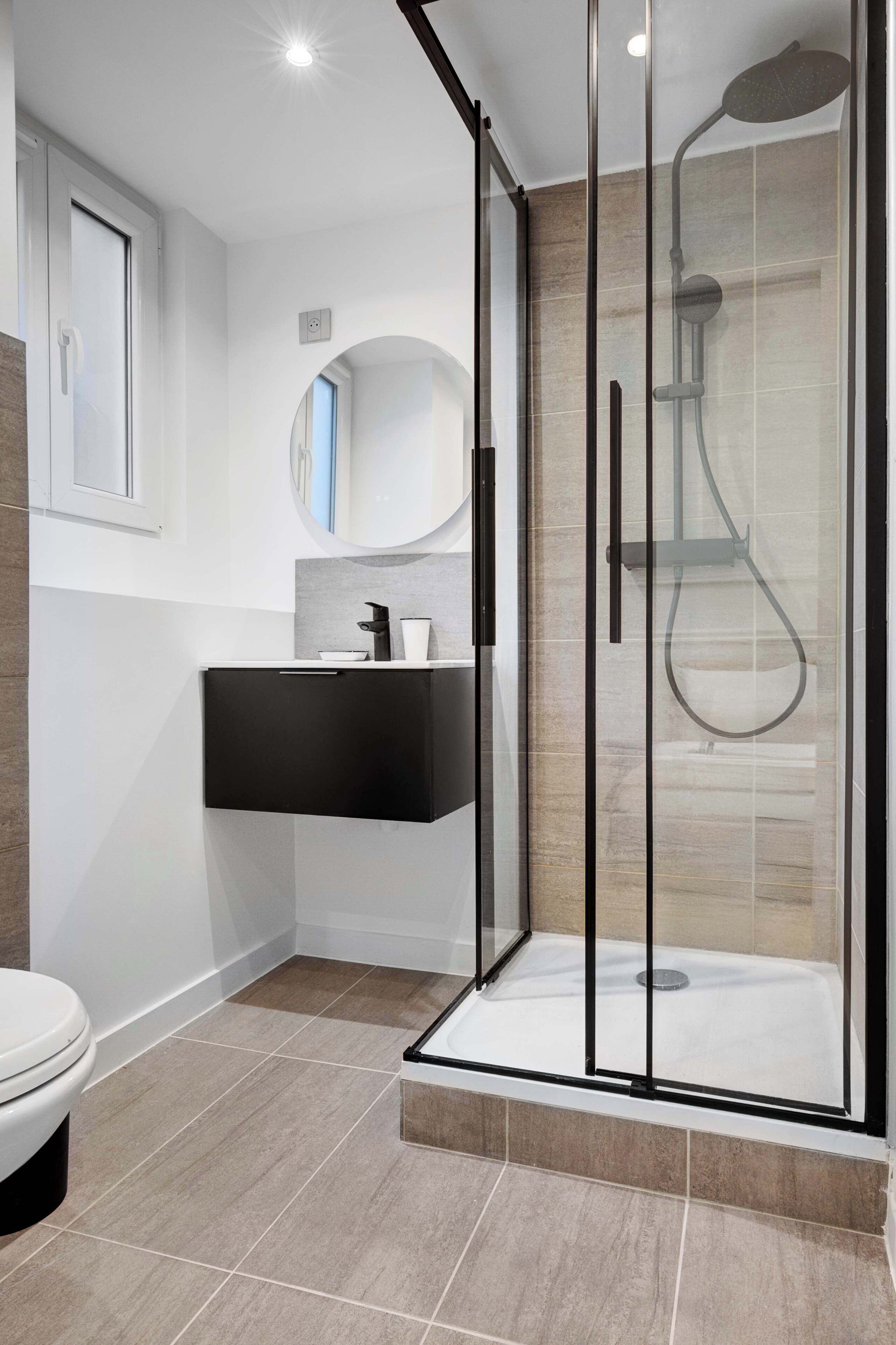 Une salle de bain moderne avec une douche à parois de verre, un meuble-lavabo noir et des toilettes blanches.