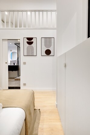 A modern bedroom with a bed, a wooden floor, and two abstract wall art pieces.