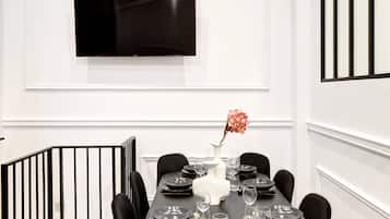 Un comedor moderno con una mesa negra dispuesta para seis comensales, paredes blancas, un televisor de pantalla plana montado y una barandilla negra.