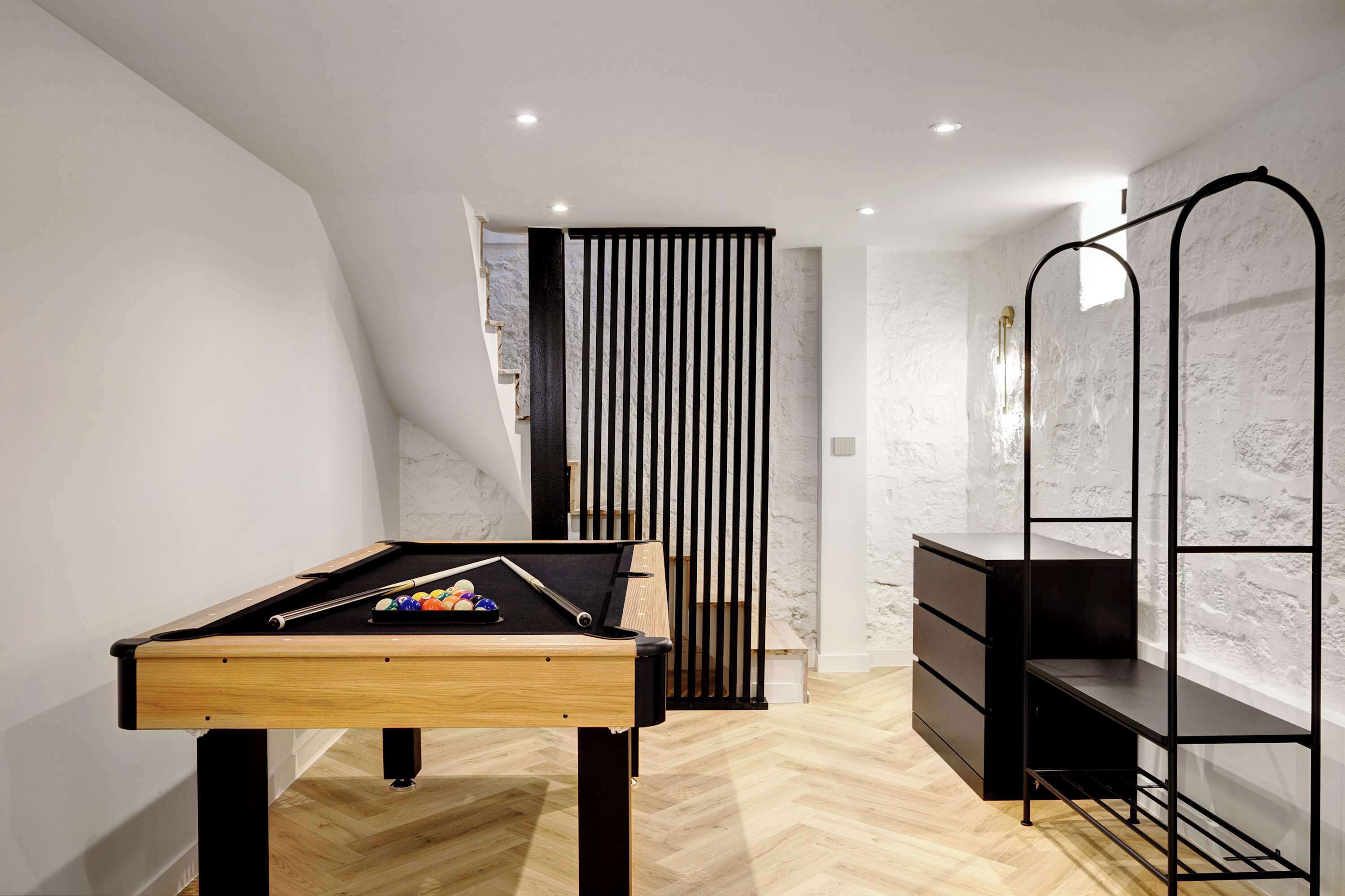 Una habitación moderna con una mesa de billar, un estante metálico negro y una pared blanca con textura.
